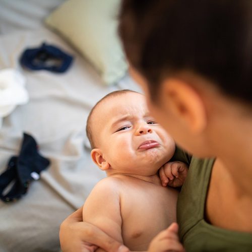 Upset and tired baby crying while his mother trying to calm him, holding baby boy in arms