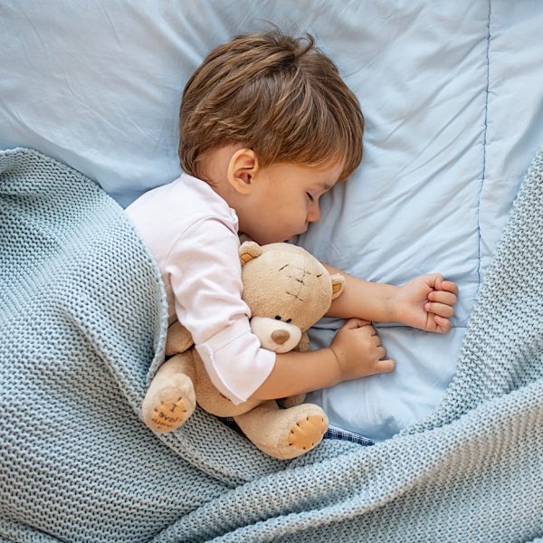 Photo of baby boy sleeping together with teddy bear. His favorite napping spot. Adorable kid boy after sleeping in bed with toy. Boy sleeping on bed with teddy bear. Sleepyhead