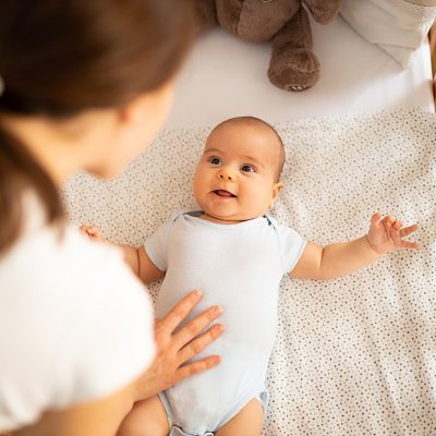 Mother leaning over side of crib and talking to her baby boy. Child looking at mum and smiling